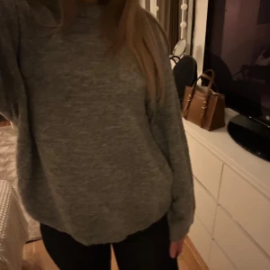 Grå stickad tröja - Mysig grå stickad tröja med långärmad design. Perfekt för kyligare dagar och enkel att matcha med olika outfits. Tröjan har en avslappnad passform och ribbade muddar vid ärmslut och nederkant.