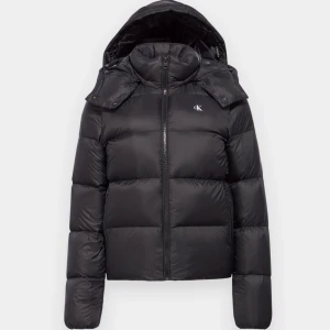 Svart dunjacka från Calvin Klein - Snygg svart dunjacka från Calvin Klein med huva och dragkedja. Jackan har en pufferdesign och är perfekt för kyliga dagar. Den har långa ärmar och en stilren look med CK-logga på bröstet.(använd endast 2-3ggr) Dm för mer info❤️‍🔥❤️‍🔥Inga defekter!!!