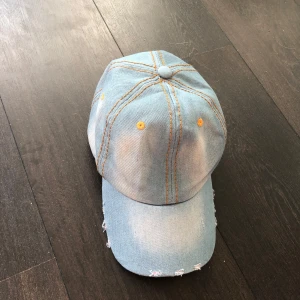Ljusblå jeanskeps med slitningar - Snygg ljusblå keps i jeansmaterial med slitna detaljer och orange sömmar. Kepsen har en justerbar rem baktill. Aldrig använd 😋