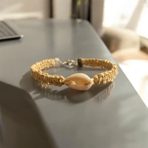 Beige armband med snäckdetalj - Charmigt beige armband med en central snäckdetalj. Armbandet är knuten med makramé med raffiagarn och har justerbart lås för perfekt passform. Perfekt för en bohemisk stil.