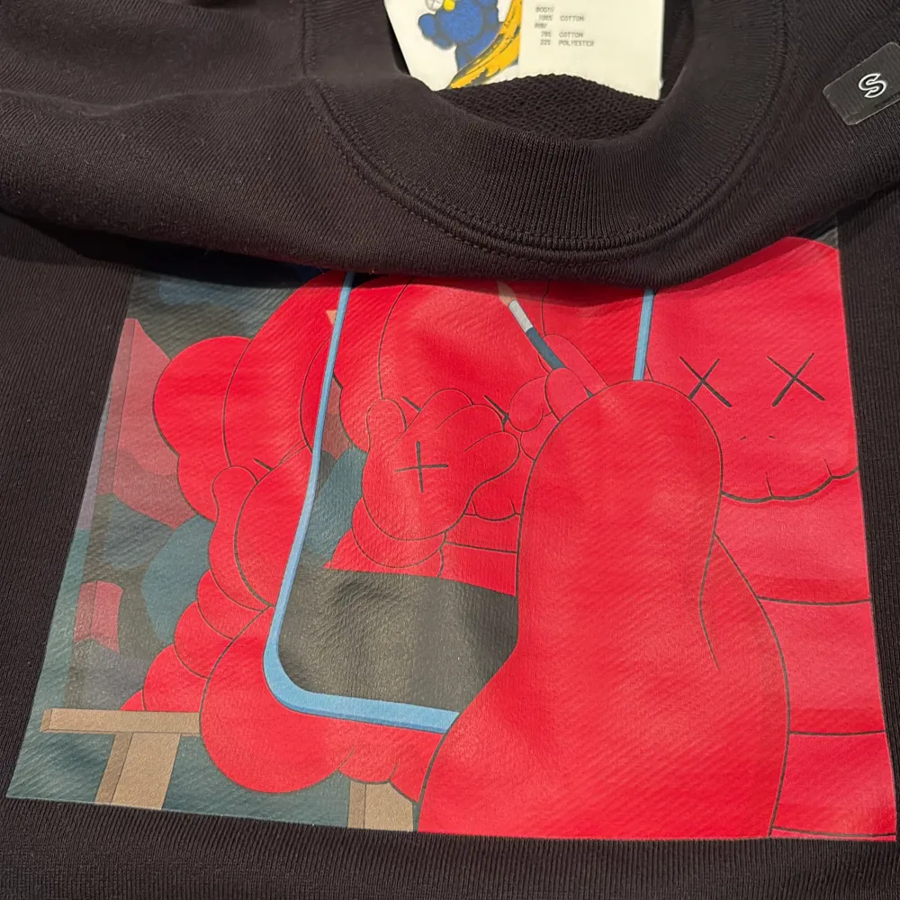 Säljer en svart sweatshirt från Uniqlo i samarbete med KAWS. Tröjan har ett färgglatt tryck med röda och blå detaljer på framsidan. Tillverkad i bomull och polyester för en bekväm passform. Perfekt för dig som gillar unik design! Helt ny. Neuletakit & Villapaidat.