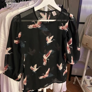 Svart blus med rosa fåglar. - Fin blus med rosa fåglar. Ganska genomskinlig med en knapp bak. 