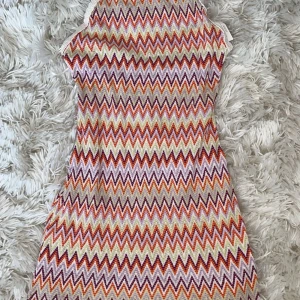 Mönstrad klänning med zigzag-mönster - Snygg klänning med färgglatt zigzag-mönster i orange, lila och beige. Klänningen har smala axelband och en öppen rygg som ger en somrig känsla. Perfekt för varma dagar! den är liten i stl och passar mig som har s
