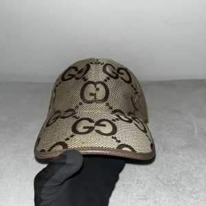 Gucci jumbo beige färg - Snygg beige keps med ett distinkt GG-mönster i brunt. Du kan ändra storleken på kepsen där bak. Perfekt för att ge din outfit en stilfull touch.