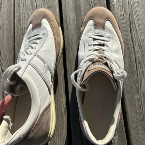 Vita och beige sneakers från Hogan Rebel - Snygga sneakers från Hogan Rebel i vitt och beige. Skorna har en klassisk design med snörning och en gummisula i brunt. Perfekta för en stilren look.