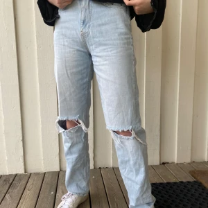 Ljusblå jeans från Gina Tricot - Säljer ett par ljusblå jeans från Gina Tricot med slitna knän för en trendig look. Jeansen har en hög midja och en straight passform. Perfekta för en avslappnad stil. Passar perfekt med tröjan modellen har på sig över som jag också säljer🌸😻❤️💗