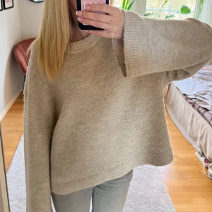 Beige stickad tröja från Gina Tricot - Säljer en mysig beige stickad tröja från Gina Tricot i premiumkvalitet. Tröjan har långa ärmar och en rund halsringning, perfekt för kyliga dagar. Den är enkel att matcha med olika outfits och ger en stilren look.