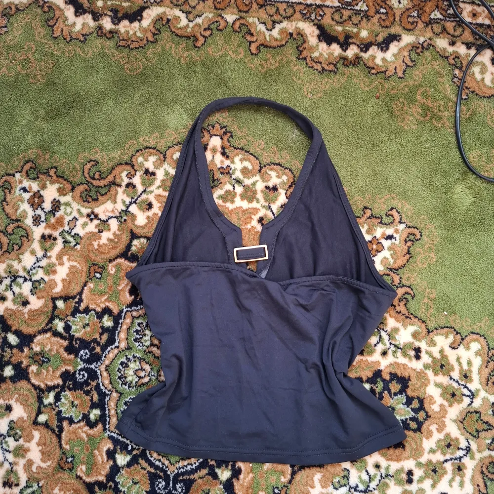Snygg svart halterneck topp med djup v-ringning. Perfekt för en stilren look. Toppen har en enkel design som gör den lätt att matcha med olika outfits.. Yläosat.