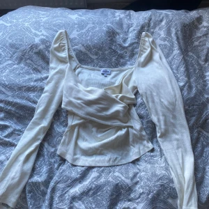 Vit ribbad topp från Bubbleroom - Säljer är vit/krämvit långärmad topp från bubbleroom. Den har en fin omlottdesign framtill vilket gör att den har en väldigt fin passform. Använd ett fåtal gånger 