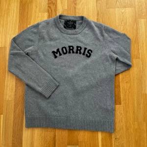 Grå tröja från Morris - Säljer en stilren grå tröja från Morris med svart text på bröstet. Tröjan har långa ärmar och ribbade muddar vid ärmslut och nederkant. Perfekt för en avslappnad look.