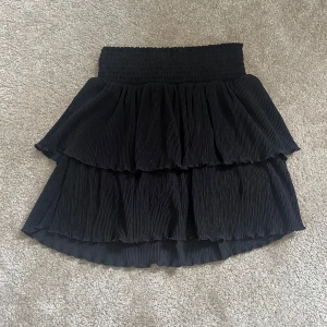 Svart volangkjol❤️ - Snygg svart kjol med volanger i flera lager. Kjolen har en elastisk midja för bekväm passform och är perfekt för att ge en chic touch till din outfit. Den plisserade designen ger en elegant känsla.