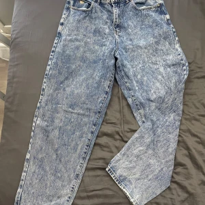 Blå baggy jeans från Butter - Säljer ett par blå baggy jeans från Butter med en cool tvättad look. De har en avslappnad passform och en unik detalj med en liten broderad figur i fickan. Perfekta för en casual stil!