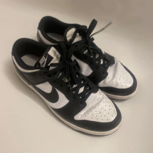 Svartvita Nike sneakers - Snygga svartvita Nike sneakers med klassisk design. Skorna har snörning och en bekväm sula, perfekt för vardagsbruk. Den ikoniska Nike-loggan syns både på sidan och hälen.