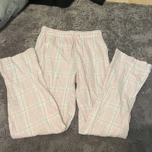 Rosa rutiga byxor - Mysiga rosa byxor med rutigt mönster i ljusblått och vitt. Har en liten brun fläck på benet, därav priset. Men om man endast har de hemma eller sover i dem spelar det kanske ingen roll. De kommer från Gina Tricot, storlek 158-164, fint skick!