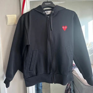 Svart hoodie från Comme des Garçons - Säljer en svart zip hoodie från Comme des Garçons med det ikoniska röda hjärtat på bröstet. Vet tyvärr inte om den är äkta då jag köpte den på plick men förra ägaren sa att den var äkta. Lite nopprig.