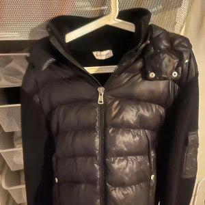 Moncler cardigan - Snygg svart dunväst från Moncler med dragkedja och huva. Västen har quiltade detaljer och ribbade ärmar. Perfekt för både våren och sommarkvällar.  Pris kan diskuteras men bara rimliga bud.