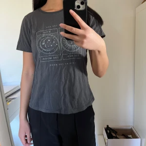Grå t-shirt med sol- och månmotiv - Snygg grå t-shirt med tryck av solen och månen i vitt. Perfekt för en avslappnad stil. Rund hals och kortärmad design.