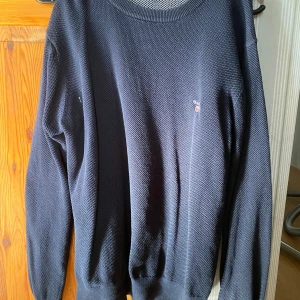 Svart stickad tröja med broderad detalj - Säljer en stilren svart stickad tröja med en liten broderad detalj på bröstet. Tröjan har långa ärmar och en rund halsringning. Perfekt för kyligare dagar.