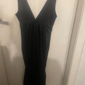 Svart balklänning med v-ringning - Säljer en svart långklänning med djup v-ringning både fram och bak. Klänningen är ärmlös och har en figurnära passform som ger en stilren och klassisk look. Perfekt för speciella tillfällen.