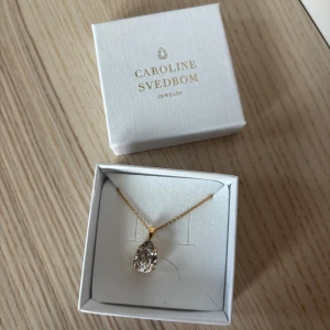 Guldhalsband med kristall från Caroline Svedbom - Elegant halsband från Caroline Svedbom med en gnistrande droppformad kristall i en guldpläterad kedja. Perfekt för att lägga till en touch av glamour till din look.