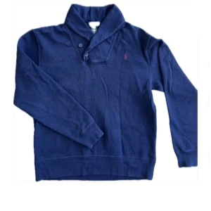 Mörkblå tröja från Ralph Lauren - Säljer en stilren mörkblå tröja från Ralph Lauren med en klassisk krage och knappar. Tröjan har ett broderat rött logotypmärke på bröstet och långa ärmar. Perfekt för en avslappnad men elegant look. Storlek L. Ny≈1000 men jag säljer min för 400kr