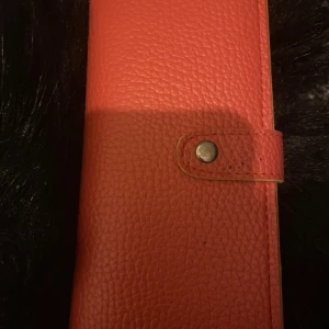 Röd plånbok i skinn - Snygg röd plånbok i skinn med en knappstängning. Perfekt för att hålla ordning på dina kort och kontanter. Använt några antal gånger men fortfarande i bra skick.