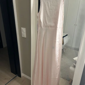 Ljusrosa långklänning - Elegant ljusrosa långklänning med omlott-design och djup v-ringning. Klänningen är ärmlös och har en mjuk, flytande passform som ger en romantisk känsla. Perfekt för speciella tillfällen.Pris kan diskuteras 