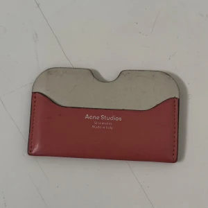 Korthållare från Acne Studios - Säljer en stilren korthållare från Acne Studios i flera färger. Framsidan är i beige och rosa, medan baksidan har en kombination av orange och rosa. Tillverkad i Italien, perfekt för att hålla kort och kontanter.