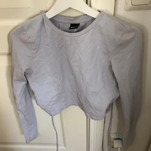 Ljusblå croppad topp från Gina Tricot - Säljer en ljusblå croppad topp från Gina Tricot med långärmad design och en öppen rygg med knytning. Perfekt för en trendig look. 💙