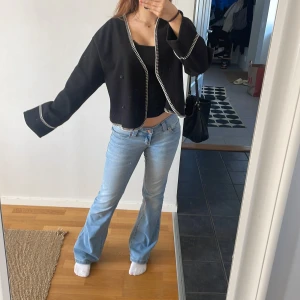 Svart omlottjacka med vita detaljer - Snygg svart omlottjacka med vita sömmar. Jackan har långa ärmar och en croppad passform. 