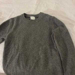 Grå stickad tröja - Säljer en mysig grå stickad tröja med rund halsringning. Perfekt för kyliga dagar och har ribbstickade muddar vid ärmslut och nederkant. Passar bra till både jeans och kjol.
