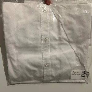 Vit skjorta från H&M - Säljer en klassisk vit skjorta från H&M. Skjortan har en stilren design med knappar framtill och en krage med kontrastfärg på insidan. Perfekt för både formella och avslappnade tillfällen.
