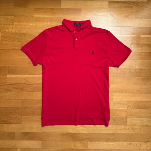 Röd pikétröja från Ralph Lauren - Säljer en klassisk röd pikétröja från Ralph Lauren med den ikoniska broderade logotypen på bröstet. Tröjan har korta ärmar och en stilren krage med knappar. Perfekt för en avslappnad men ändå stilfull look. Passa på att köpa denna tidlösa favorit! 🔥Nästan aldrig använd och är i mycket fint skick