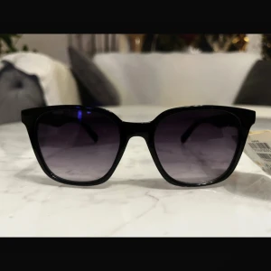 Svarta solglasögon från Foster Grant - Snygga svarta solglasögon från Foster Grant med en klassisk design. De har en lätt oversized passform och mörka linser som ger 100% UVA/UVB-skydd. Perfekta för soliga dagar!