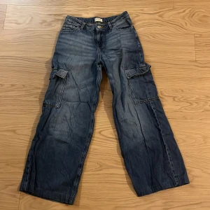 Blå cargopants från Lindex - Säljer ett par blå cargopants från Lindex med flera praktiska fickor och en avslappnad passform. Byxorna har en klassisk cargostil med breda ben och är perfekta för en casual look. De har en knapp och dragkedja framtill.