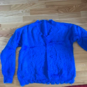 Blå fluffig tröja - Säljer en supermjuk och fluffig blå tröja med långa ärmar. Perfekt för att hålla sig varm och mysig. Tröjan har en enkel design utan mönster och är gjord i ett syntetmaterial som ger en skön känsla. Passar perfekt för kyliga dagar.