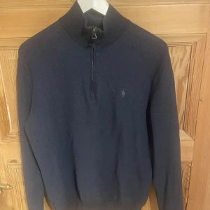 Mörkblå tröja från Polo Ralph Lauren - Säljer en stilren mörkblå tröja från Polo Ralph Lauren i fin bomull. Tröjan har en dragkedja vid halsen och en diskret logga på bröstet. Perfekt för en avslappnad men ändå elegant look.