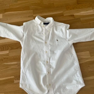 Vit skjorta från Ralph Lauren - Säljer en klassisk vit skjorta från Ralph Lauren med broderad logotyp på bröstet. Skjortan har långa ärmar och knappar framtill. Perfekt för en stilren look. Tar även byten !! Med andra saker med 