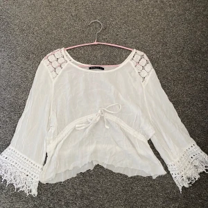 Vit blus  - Säljer en vit blus från Mirelle med vackra spetsdetaljer och knytning framtill. Blusen har trekvartsärmar och en luftig passform, perfekt för varma dagar. Den har även dekorativa fransar vid ärmslut och nederkant.