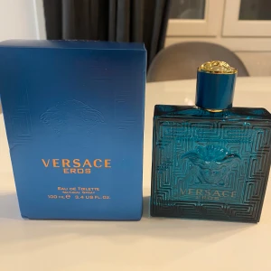 Versace Eros Eau de Toilette 100 ml - Säljer en Versace Eros Eau de Toilette i en elegant blå flaska med guldlock och Medusa-motiv. Flaskan rymmer 100 ml och har en stilren design med geometriska mönster. Perfekt för den som vill ha en doft med karaktär och stil.