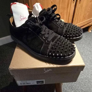 Svarta sneakers med nitar från Christian Louboutin - Snygga svarta sneakers i mocka från Christian Louboutin med coola nitar på tån och klassisk röd sula. Skorna har snörning och en stilren design som sticker ut. Perfekta för dig som vill ha något unikt i garderoben. Onlinekvitto och så är sulan lite sliten därför priset. Priset är därför inte hugget i sten🪨⛏️ Skriv gärna till mig vid funderingar😀