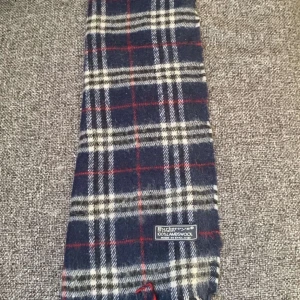 Rutig halsduk från burberry - Säljer en  rutig halsduk i blått, vitt och rött från burberry . Halsduken är tillverkad i mjuk ull och har en tidlös design som passar perfekt för våren