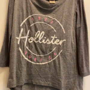 Grå tröja från Hollister - Säljer en grå tröja från Hollister med tryck i vitt och rosa. Tröjan har trekvartsärmar och en avslappnad passform. Perfekt för en casual look! Den är från Hollister i storlek XS