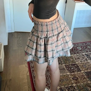 Rutig kjol - Rutig volangkjol, liknar Burberry. Stretchig midja. Midjemått: 66-86 cm, 33-43 cm mätt rakt över. Längd: 40 cm