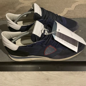 Phillipe modell trainers - Skick 9/10  trainers i storlek 45 . Phillipe modell boxen samt tagsen och dustbag följer självklart med det vill säga allt OG.  Snygga marinblå sneakers från Philippe Model med vita och svarta detaljer. Skorna har en broderad logga på sidan och snörning framtill. Perfekta för en stilren look.använda några gånger