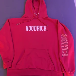 Röd hoodie från Hoodrich - Säljer en snygg röd hoodie från Hoodrich med tryck både fram och på ärmen. Den har en klassisk känguruficka och justerbar huva med dragsko. Perfekt för en avslappnad stil.