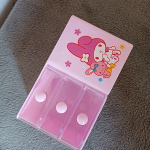 Rosa sminkförvaring med tecknat motiv - Söt rosa sminkförvaring med tre genomskinliga lådor och ett öppet fack. Perfekt för att organisera smink som läppstift, ögonskugga och sminkborstar. Har ett gulligt tecknat motiv på sidan.