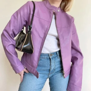 Lila skinnjacka -  Lila skinnjacka (skinnimmitation), med dragkedja och knappdetalj vid halsen.  Inköpt på Plick, säljer vidare då den tyvärr är för liten för mig. Bilderna är från tidigare säljare! 