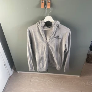 Grå hoodie från Peak Performance - Säljer en stilren grå hoodie från Peak Performance. Tröjan har en dragkedja framtill och en bekväm huva. Perfekt för en avslappnad stil.