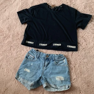 Blå jeansshorts från Name It - Snygga blå jeansshorts från Name It med slitna detaljer och upprullade benslut. Shortsen har klassisk femficksdesign, knapp och dragkedja framtill samt resår i midjan för extra komfort. Perfekta för varma dagar och en avslappnad stil.